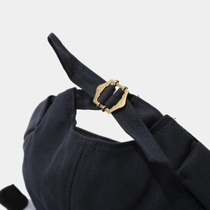 Close-up of black canvas cap with adjustable vintage bronze metal buckle detail