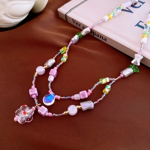 Double-layer beaded necklace with pink glass flowers and green leaf charms on velvet