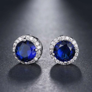 Macro shot of round halo stud earrings with dark blue center stone and silver base