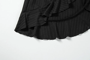 Detailed close-up of black ribbed knit fabric with soft ruffled hem and texture