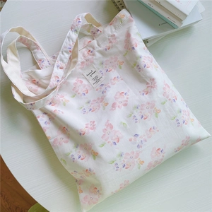 Detail shot of a canvas tote bag with pink floral print and woven label on a white table