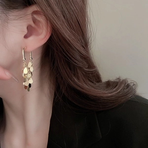 Close-up of tiered gold sequin tassel earrings on model with polished metallic texture