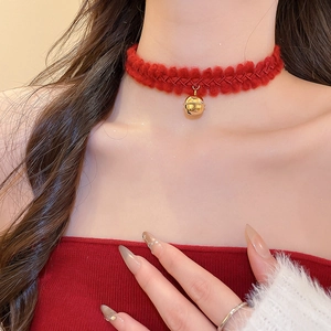 Détail d'un ras-de-cou en tricot rouge avec pendentif cloche dorée sur un mannequin