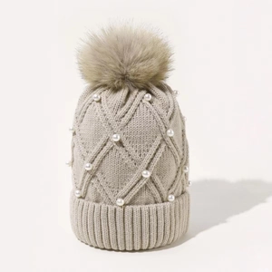 Detail of beige knit beanie with large pompom, diamond pattern, and white pearl accents