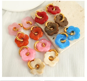 Flat lay of colorful floral hoop earrings in various shades on a textured stone tray