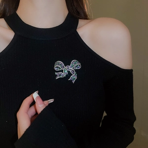 Detail view of a luxury zircon bow brooch with purple and green stones on a black sweater