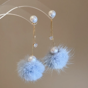 Macro shot of sky blue pompom earrings with white pearls and gold tassel details