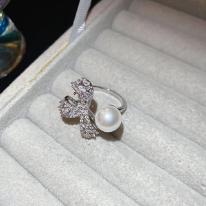 Detail of zircon bow pearl open ring on gray velvet display case with silver finish