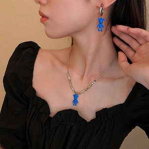 Detailed view of Klein blue bear pendant necklace and matching earring on model