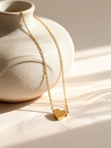 Close-up of a 3D heart pendant necklace in 18K gold finish on a decorative ceramic pot
