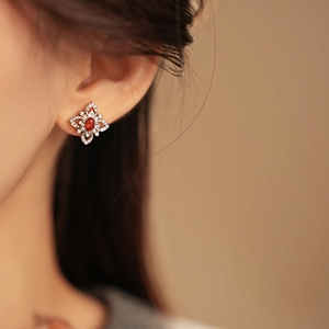 Close-up of silver flower stud earring with a red gemstone and micro-set zircons on ear