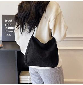 Detailed back view of a large black corduroy tote bag worn by a model in a cozy setting