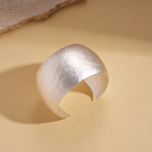 Close-up of a silver wide open bangle featuring a unique hammered metal texture finish