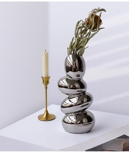 Detail of silver mirrored pebble-shaped vase with creative stacked design and leaf branch