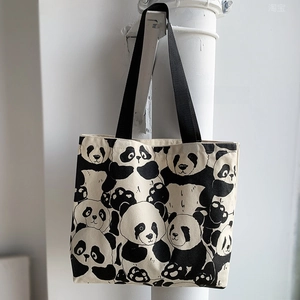 Detailed close-up of a panda print canvas tote bag with black strap hanging on a white wall