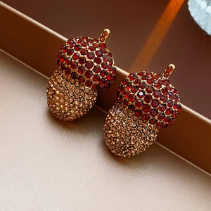 Detail of acorn earrings with red and champagne crystals on a gold metal tray