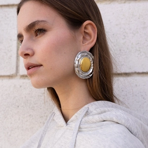 Macro detail of large two-tone geometric earrings on model with gold and silver texture