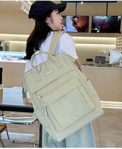 Close-up of a light green backpack featuring a white fashion label and bear embroidery