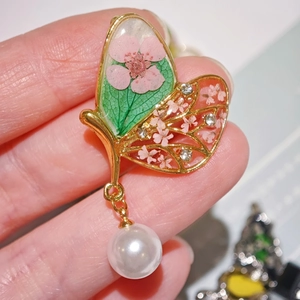 Détail d'une broche papillon dorée avec fleurs séchées roses et une perle blanche ronde