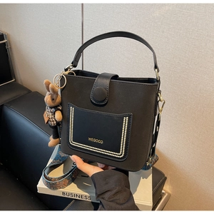Detail of black bucket bag with gold bead trim, woven strap and plush bunny charm