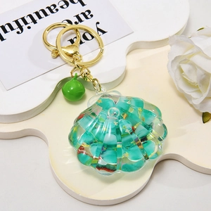 Macro detail of a green shell-shaped liquid oil keychain with small beads and a gold bell