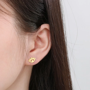 Close-up of a gold-toned evil eye stud earring with eyelash details on a female model