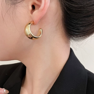 Close-up of a model wearing minimalist thick golden C-shaped hoop earrings