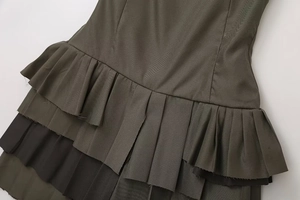 Detailed close-up of dark olive green pleated fabric on a tiered spaghetti strap dress