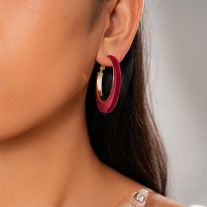 Detail of large C-shaped earrings with dark red velvet coating and golden metal interior