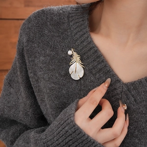 Detailed view of a gold feather brooch with white mother-of-pearl and zircon inlay