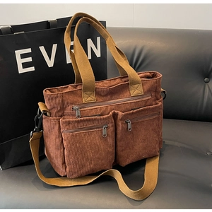 Detail of dark brown corduroy tote bag showing metal zippers and textured front pockets