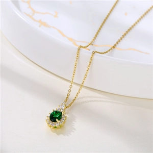 Golden necklace with green oval crystal pendant on a white ceramic display plate