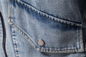 Detailed macro view of denim jacket chest pocket with metal button and orange stitching