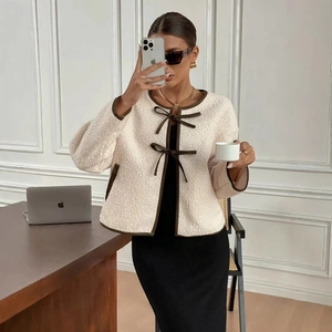 Veste élégante en tweed crème avec bordure marron et nœuds papillon portée par un mannequin