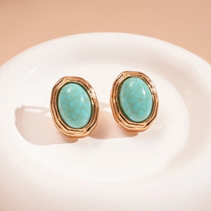 Close-up of vintage oval turquoise earrings with wave-textured gold metal edges on a dish
