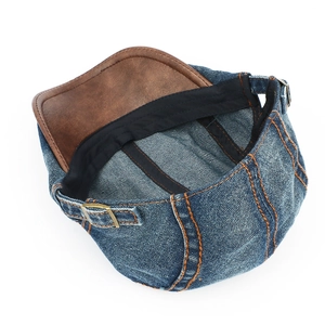 Detail of blue denim ivy cap with orange stitching and brown leather brim and adjustable strap