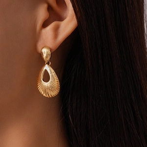Detailed close-up of golden teardrop earring with radial metallic texture on a model