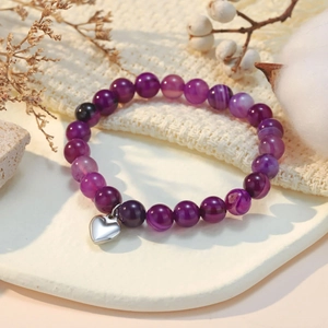Detail of purple natural stone beaded bracelet with silver heart charm on rustic fabric