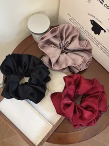 Three oversized satin scrunchies in black, champagne, and burgundy on a tray