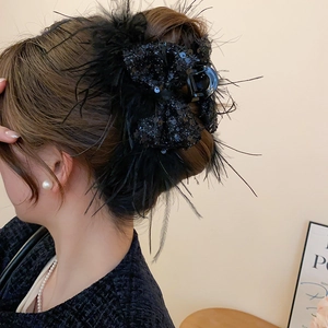 Detail of black feather and sequin bow hair claw clip worn on a bun hairstyle