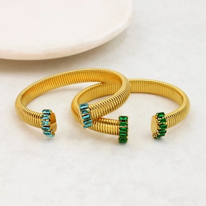 Dettaglio di bracciali a spirale dorati a C con zirconi rettangolari blu e verdi