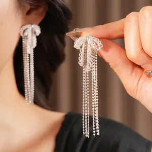 Silver bow tassel earrings with white cubic zirconia worn by model on red velvet