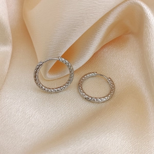 Close-up of silver titanium steel hoop earrings with hammered texture on silk fabric