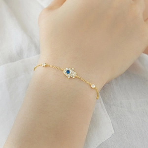 Detailed view of a gold Hamsa Hand bracelet with blue eye and sparkling clear crystals