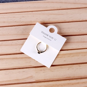 Elegant gold ring with dark gemstone on a white jewelry display card over wood texture