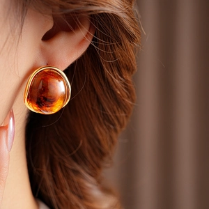 Close-up of retro amber resin round earrings with gold metal trim on model's ear