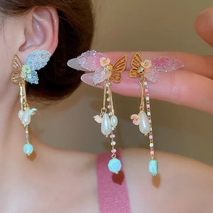 Detailed shot of butterfly tassel earrings with pearls and blue faceted beads on a model