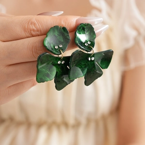 Detail of dark green resin flower earrings with crystals held by hand for scale