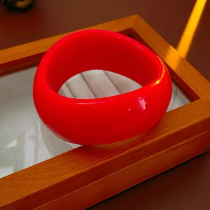 Detail of red irregular wave wide bangle with high-gloss resin finish on wooden tray