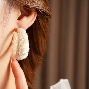 Detailed close-up of beige woven fabric C-shaped earrings worn by a model